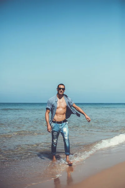 Junger muskulöser Mann, der sich ausruht und am Strand posiert. ein junger Mann geht am Meer entlang — Stockfoto
