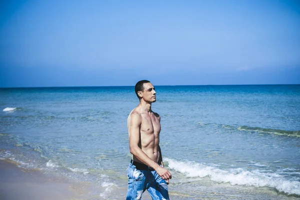 young muscular man resting and posing on the beach. A young man walks by the sea