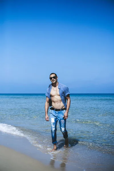 Joven musculoso descansando y posando en la playa. Un joven camina junto al mar — Foto de Stock