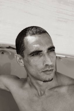 Genç kaslı adam sahilde dinleniyor ve poz veriyor.