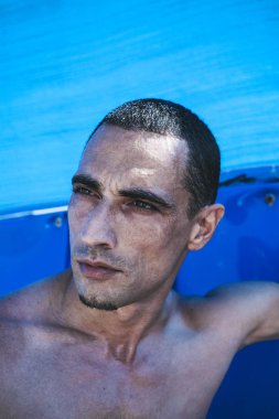 Genç kaslı adam sahilde dinleniyor ve poz veriyor.