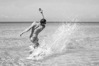 Genç kaslı adam denizde poz veriyor ve su sıçratıyor.