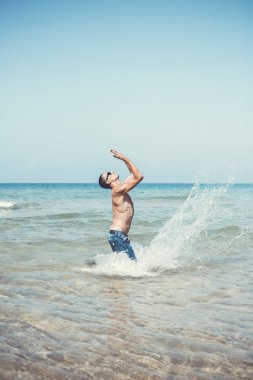 Genç kaslı adam denizde poz veriyor ve su sıçratıyor.