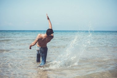 Genç kaslı adam denizde poz veriyor ve su sıçratıyor.