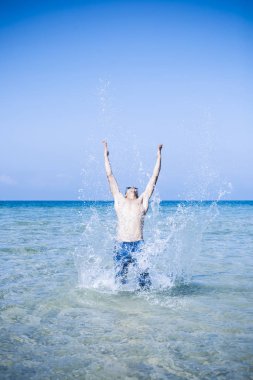 Genç kaslı adam denizde poz veriyor ve su sıçratıyor.