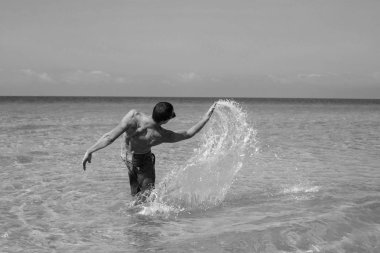 Genç kaslı adam denizde poz veriyor ve su sıçratıyor.