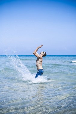 Genç kaslı adam denizde poz veriyor ve su sıçratıyor.