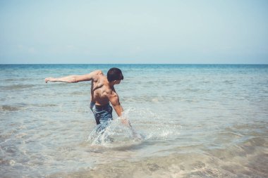 Genç kaslı adam denizde poz veriyor ve su sıçratıyor.
