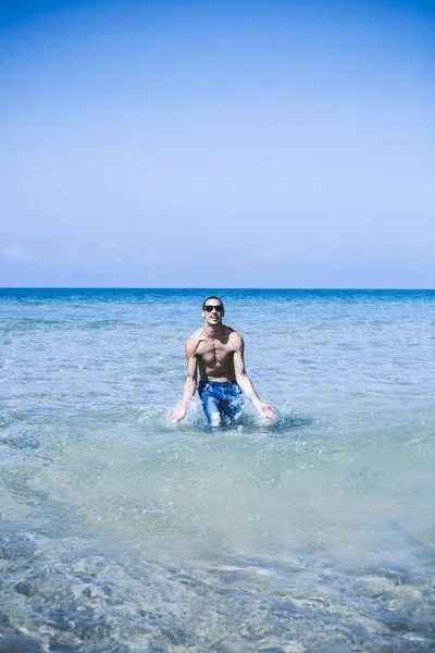 Jovem homem muscular posando e salpicando ao redor no mar — Fotografia de Stock