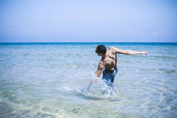 Giovane uomo muscoloso in posa e spruzzi in giro per il mare — Foto Stock