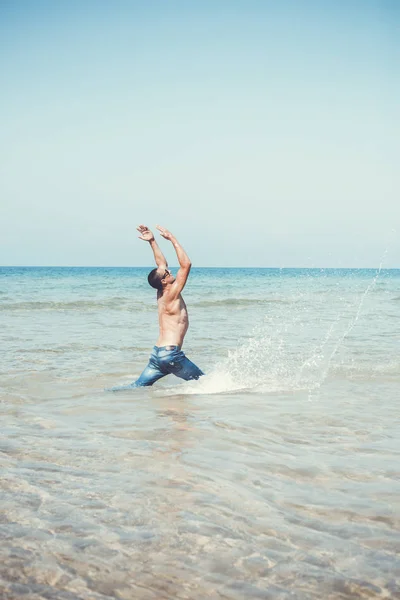 Jeune homme musclé posant et éclaboussant dans la mer — Photo