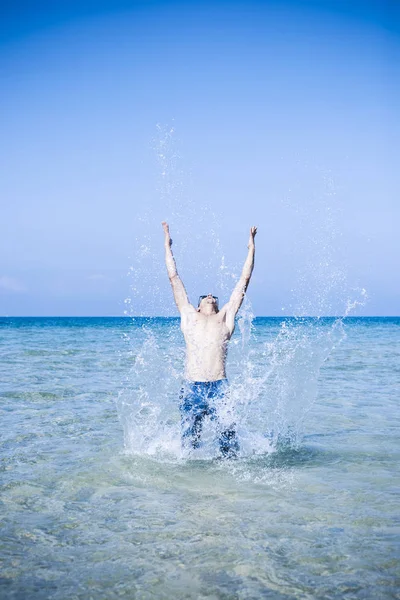 Jonge gespierde man poseren en spetteren rond in de zee — Stockfoto