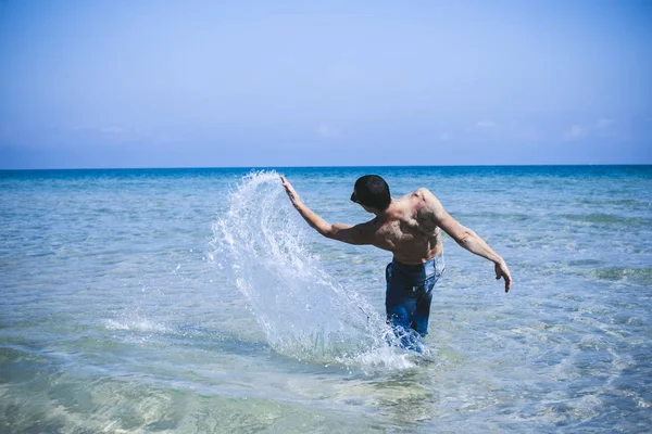 Jeune homme musclé posant et éclaboussant dans la mer — Photo