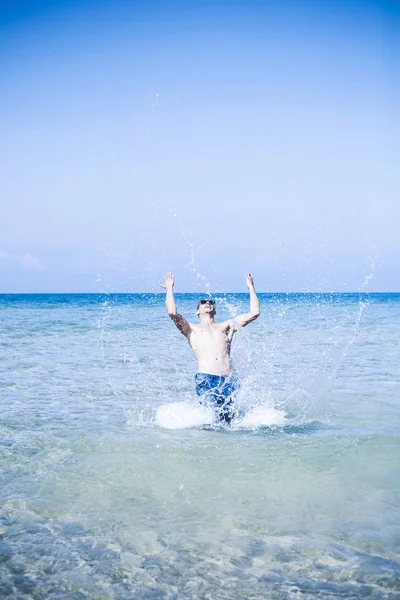 Jonge gespierde man poseren en spetteren rond in de zee — Stockfoto