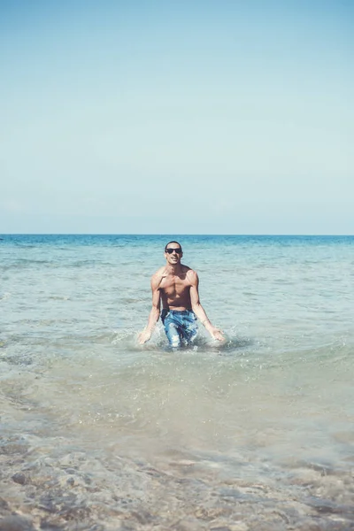 Mladý svalnatý muž pózuje a cáká kolem v moři — Stock fotografie