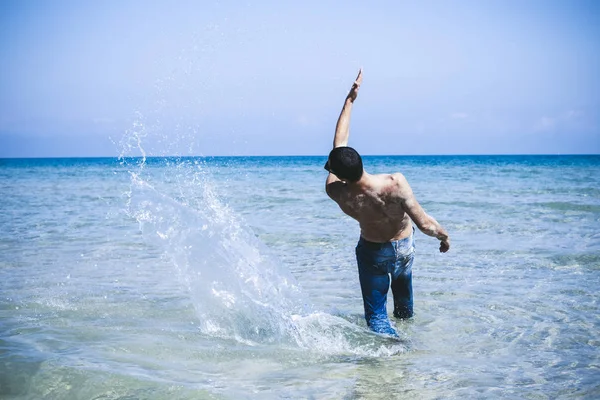 Joven musculoso posando y salpicando en el mar — Foto de Stock