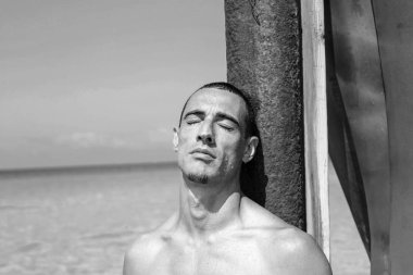 Genç kaslı adam sahilde dinleniyor ve poz veriyor.