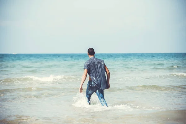 Молодий м'язистий чоловік відпочиває і позує на пляжі. Молодий чоловік ходить біля моря — стокове фото