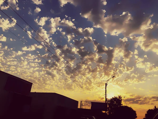 Закат облачного неба с живописными облаками, освещенными теплым солнечным светом заката. Загородная дорога на закате — стоковое фото