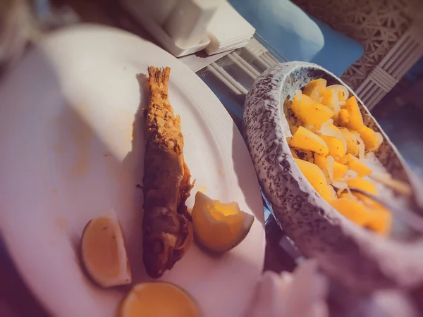 Sült hal egy tányéron citromszeletekkel. Sült burgonya hagymával a háttérben — Stock Fotó