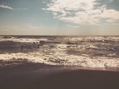 Gün batımında deniz manzarası. İnsanlar denizde yüzer. Kumlu bir sahilde parıltı lı dalgalar. Yaz güneşli gün, su arka plan