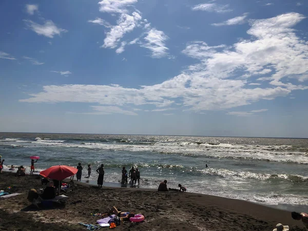 Výhled na moře během západu slunce. Lidé plavou v moři. Třpytu na písečné pláži. Letní slunný den, vodní zázemí — Stock fotografie