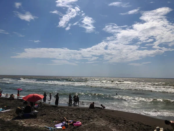 Blick auf das Meer bei Sonnenuntergang. Menschen schwimmen im Meer. glitzernde Wellen an einem Sandstrand. Sommer sonniger Tag, Wasser Hintergrund — Stockfoto