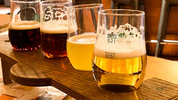 Óculos com diferentes tipos de cerveja artesanal em um bar de madeira. Bata a cerveja em uma caneca em uma fileira. Copos close-up de diferentes tipos de cerveja em um pub . — Fotografia de Stock