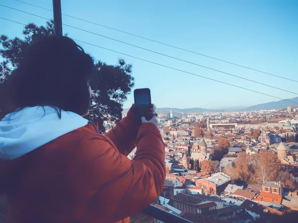穿着红色夹克的女孩在拍摄城市的照片。 具有现代地域的旧区风景秀丽 — 图库照片