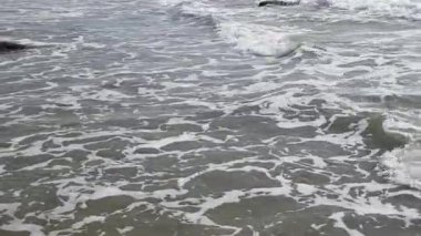 Yuvalanan deniz dalgaları kıyıya yakın büyük çıkıntılı taşları yıkıyor.