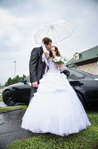 Молодята під дощем з парасолькою біля машини — стокове фото