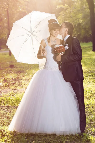 Newlyweds in the park with an umbrella — Stock Photo, Image