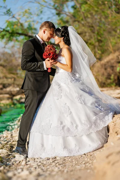 Mariage. Mariés avec un bouquet de fleurs artificielles rouge designer — Photo