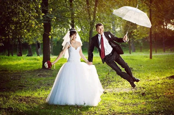 Recém-casados no parque com um guarda-chuva — Fotografia de Stock