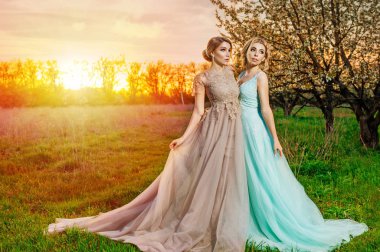 Uzun elbiseler çiçek açan ağaçlar bahçede poz'de iki kız