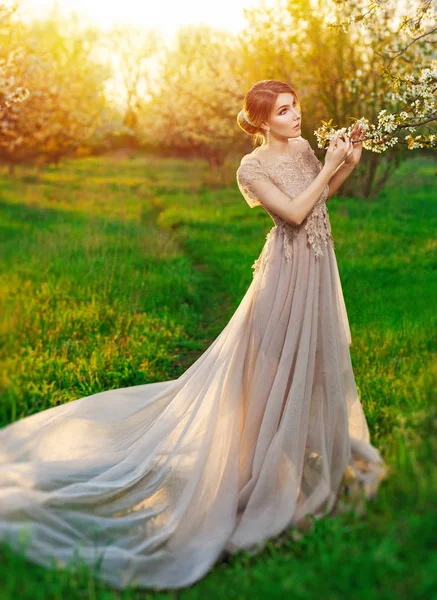 A girl in a long beige dress posing in the garden of blooming trees — Stock Photo, Image