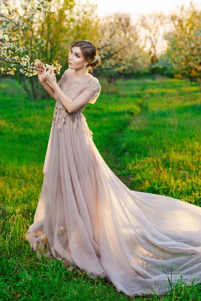 A girl in a long beige dress posing in the garden of blooming trees — Stock Photo, Image