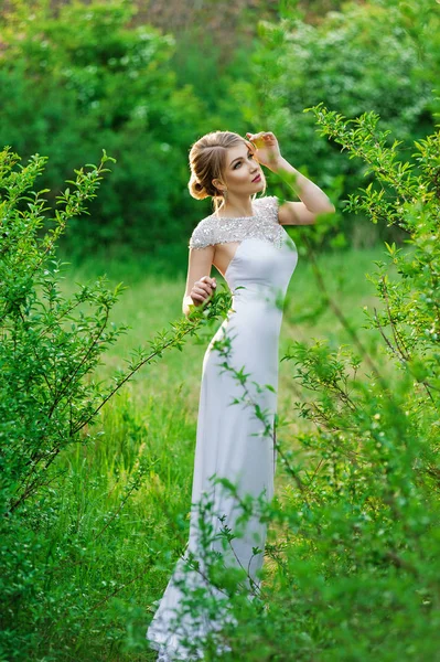 Elegant fashion model in a long white dress posing in the park — Stock Photo, Image