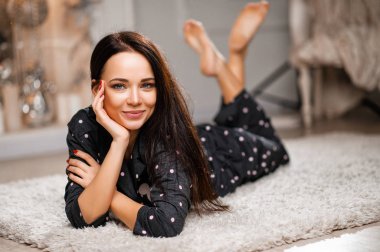 Şirin, şık esmer, pijamalı şöminenin yanındaki halıda.