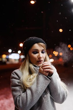 Sokakta akşam vakti şapkalı güzel bir sarışın. Makyajlı bir kızın kış portresi.