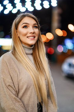 Çekici sarışın, gece şehrinin arka planında poz veriyor.