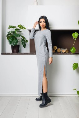 Beyaz bir duvar ve şöminenin arka planında elbiseyle poz veren çekici bir esmer.