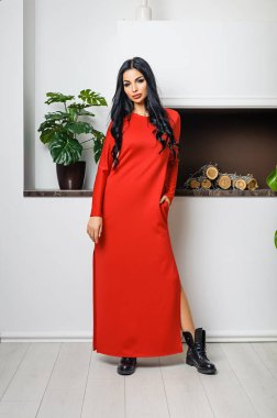 Beyaz bir duvar ve şöminenin arka planında elbiseyle poz veren çekici bir esmer.