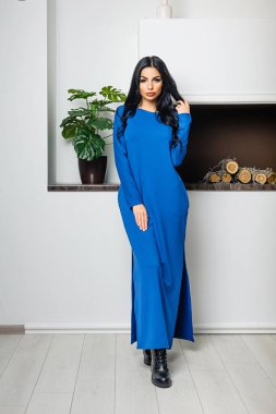 Beyaz bir duvar ve şöminenin arka planında elbiseyle poz veren çekici bir esmer.