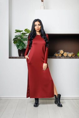 Beyaz bir duvar ve şöminenin arka planında elbiseyle poz veren çekici bir esmer.