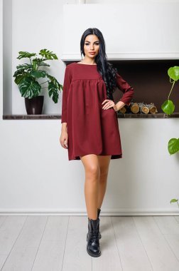 Beyaz bir duvar ve şöminenin arka planında elbiseyle poz veren çekici bir esmer.