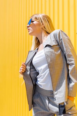 Gözlüklü sarışın ve sarı duvarlı gri takım elbiseli.