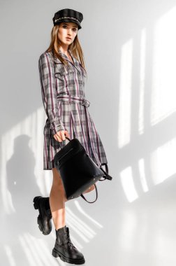 Beyaz arka planda gri kareli elbiseli çekici kahverengi saçlı kadın. Bir giyim kataloğu için fotoğraf çekinme