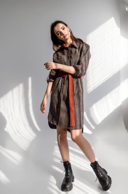 Beyaz arka planda gri kareli elbiseli çekici kahverengi saçlı kadın. Bir giyim kataloğu için fotoğraf çekinme