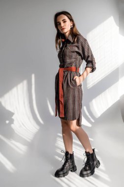 Beyaz arka planda gri kareli elbiseli çekici kahverengi saçlı kadın. Bir giyim kataloğu için fotoğraf çekinme